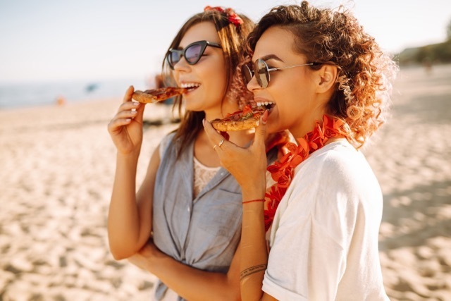 Two women eating pizza on the beach