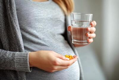 pregnant women holding glass of water and supplements