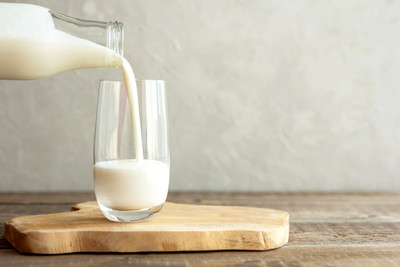 pouring a glass of milk with glass sitting on top of wooden cutting board